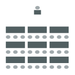 Rows of desks with chairs behind each desk facing a single desk and chair at the front of the room.