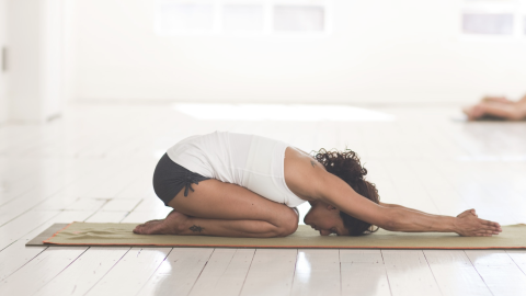 woman in child's pose on yoga mat and white floor