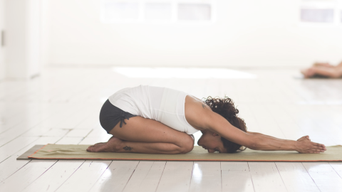 photo of woman in child's pose on mat in white room